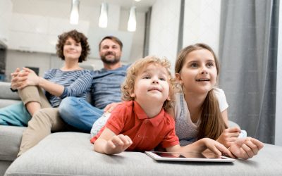 Portrait of happy family with two kids  watching TV together sitting on sofa in living room, focus on brother and sister in foreground